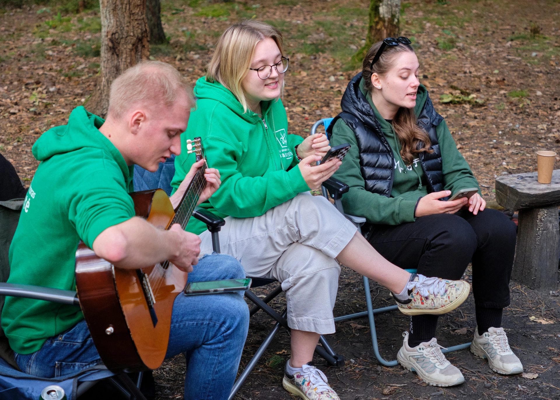 Trys choristai dainuoja dainą, vienas iš jų groja gitara